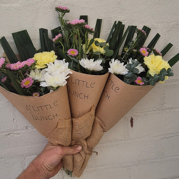 Three small flower bouquets in kraft paper cones held against a white brick wall.